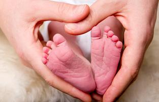 Händer bildar ett hjärta runt en nyfödds fötter.