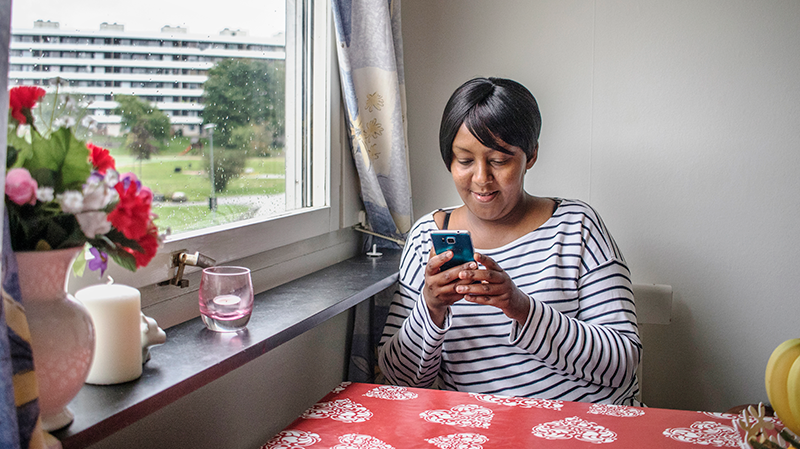 Ung kvinna sitter vid köksbordet och tittar i sin mobil