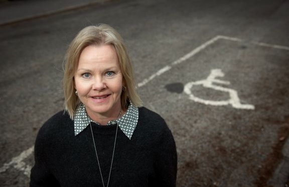 En blond kvinna står vid kanten av en parkeringsplats för personer med funktionsnedsättning.