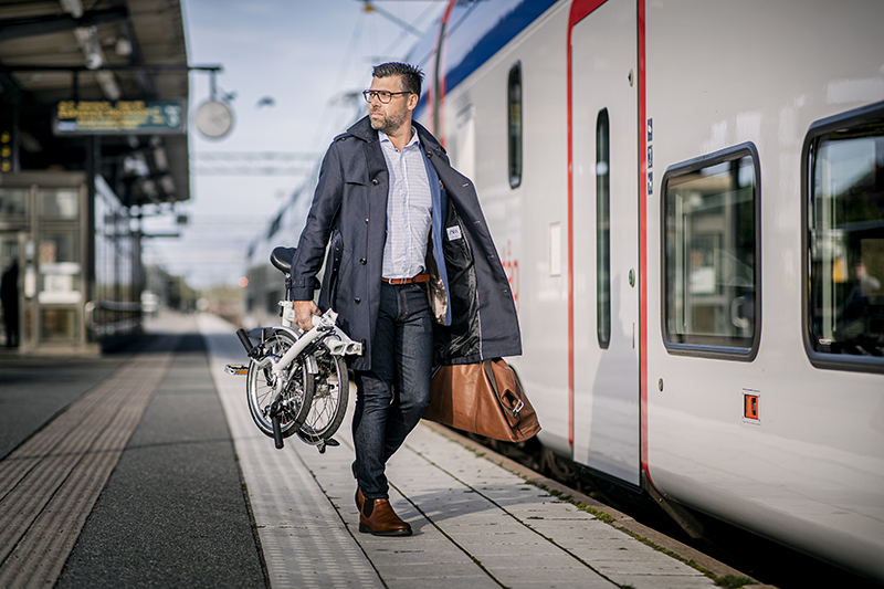 Man går på en tågperrong med en vikcykel i handen