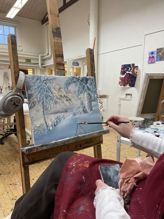 En hand som håller i en pensel och målar ett vinterlandskap