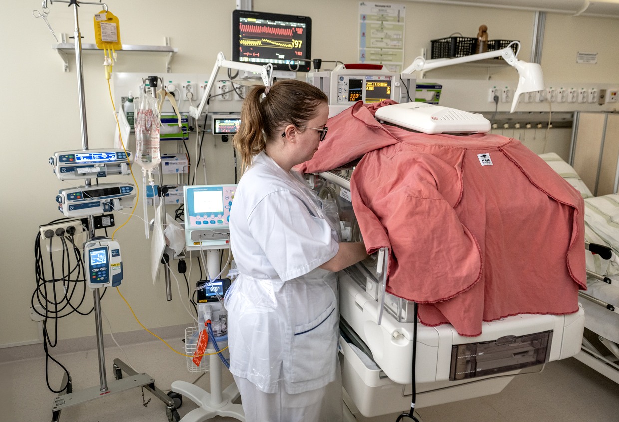 En kvinna i vårdkläder står i ett rum på neonatalavdelningen.  Hon har händerna in i en kuvös. 