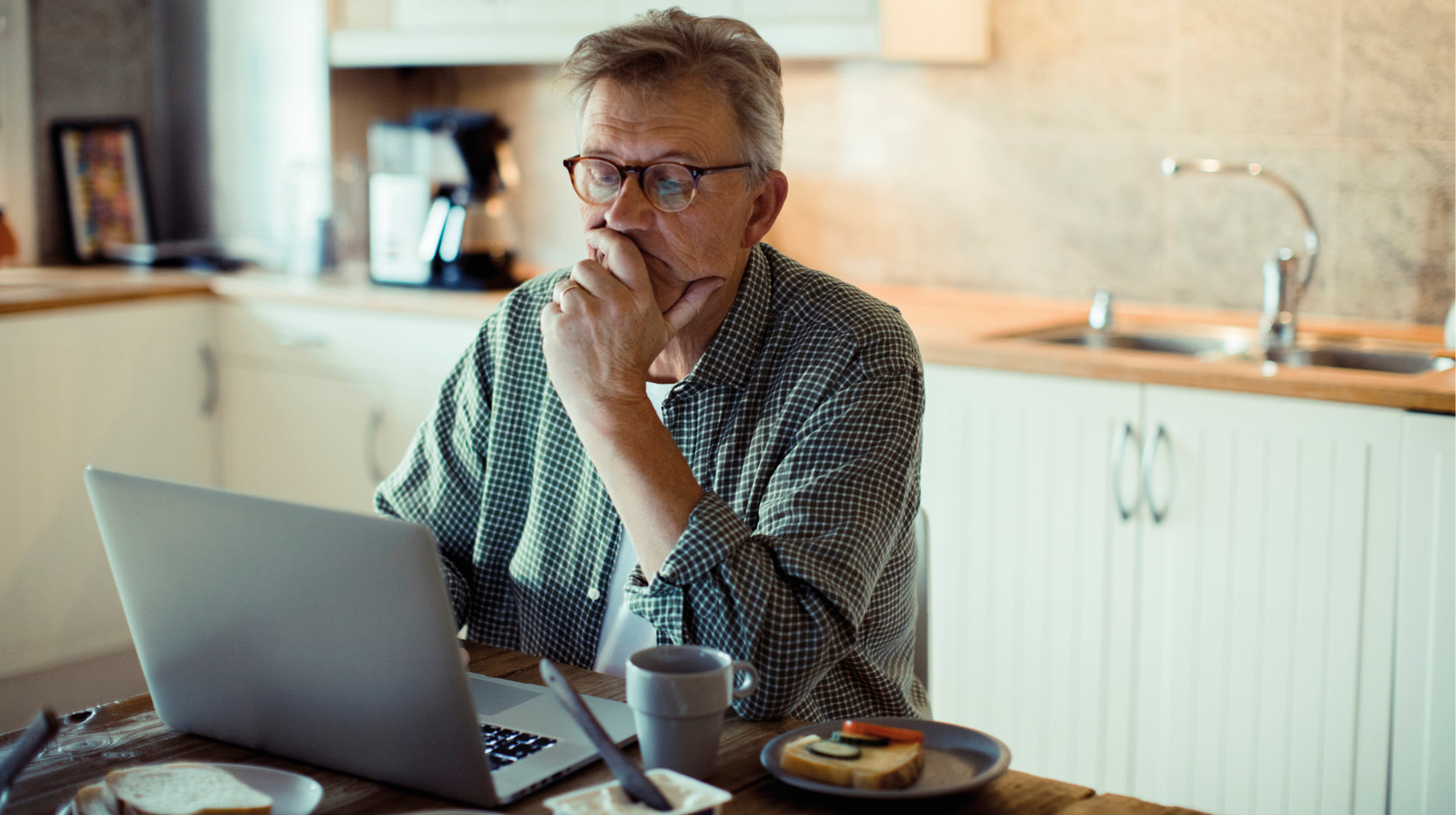 Man med bärbar dator på köksbordet